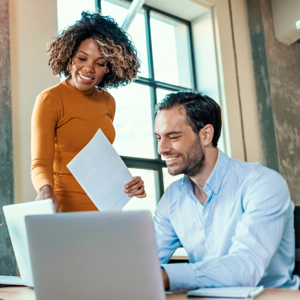 two smiling business people looking at a laptop screen.