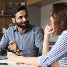 Two workers in conversation while seated at a work table.