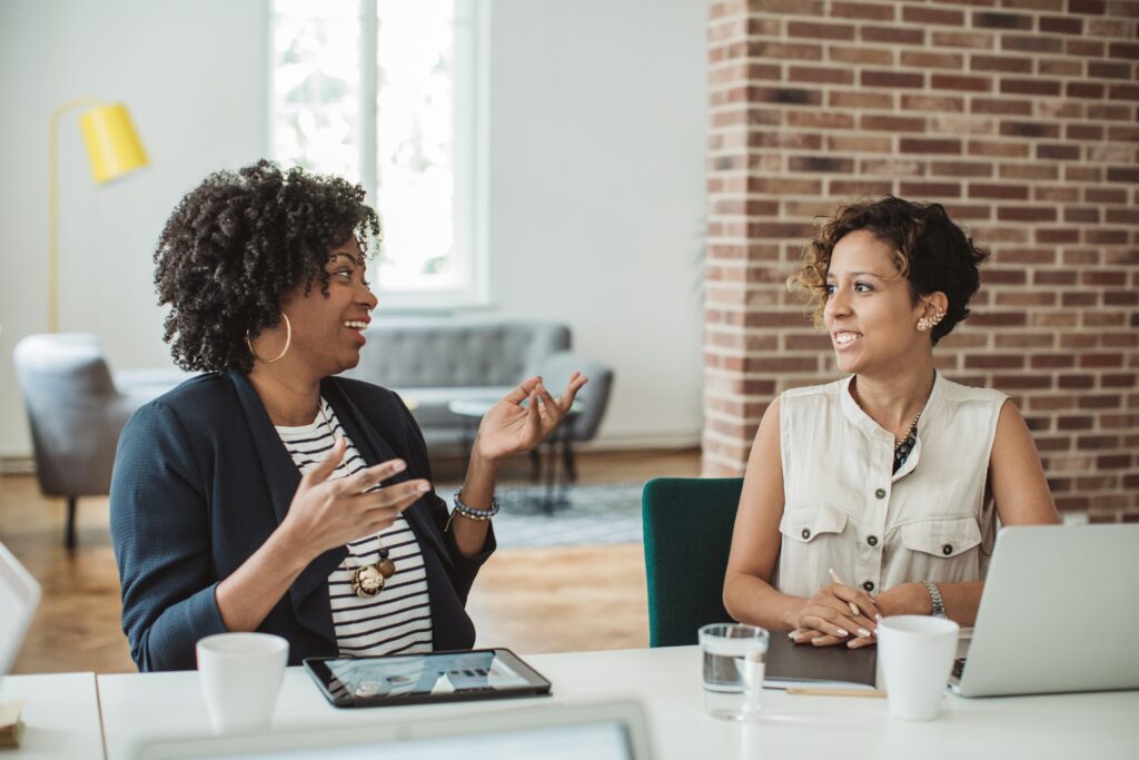 Two women seated talking while seated at a meeting table.