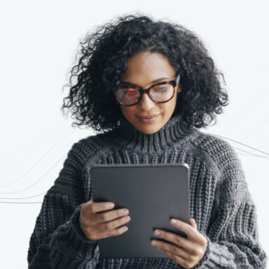 A woman wearing glasses holding a tablet and looking at the screen.