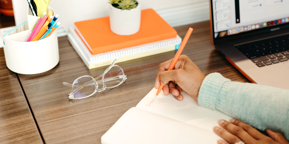 A person sits at a desk and writes in a notebook