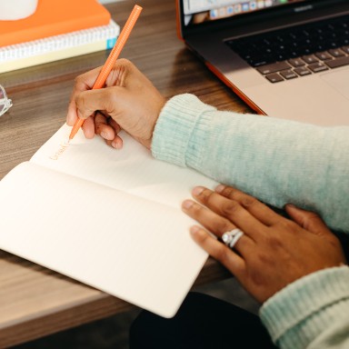 A person sits at a desk and writes in a notebook