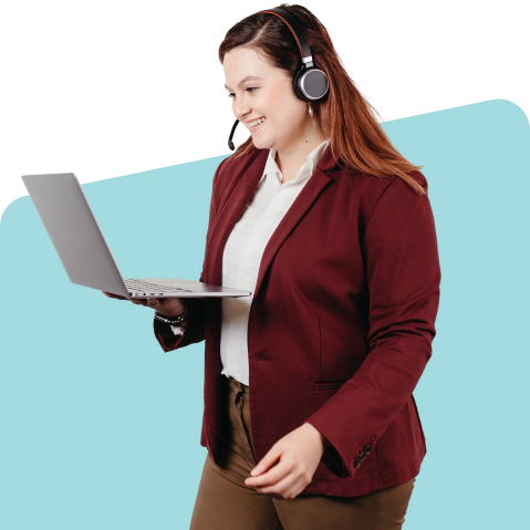 A woman standing, holding a laptop and wearing a headset.