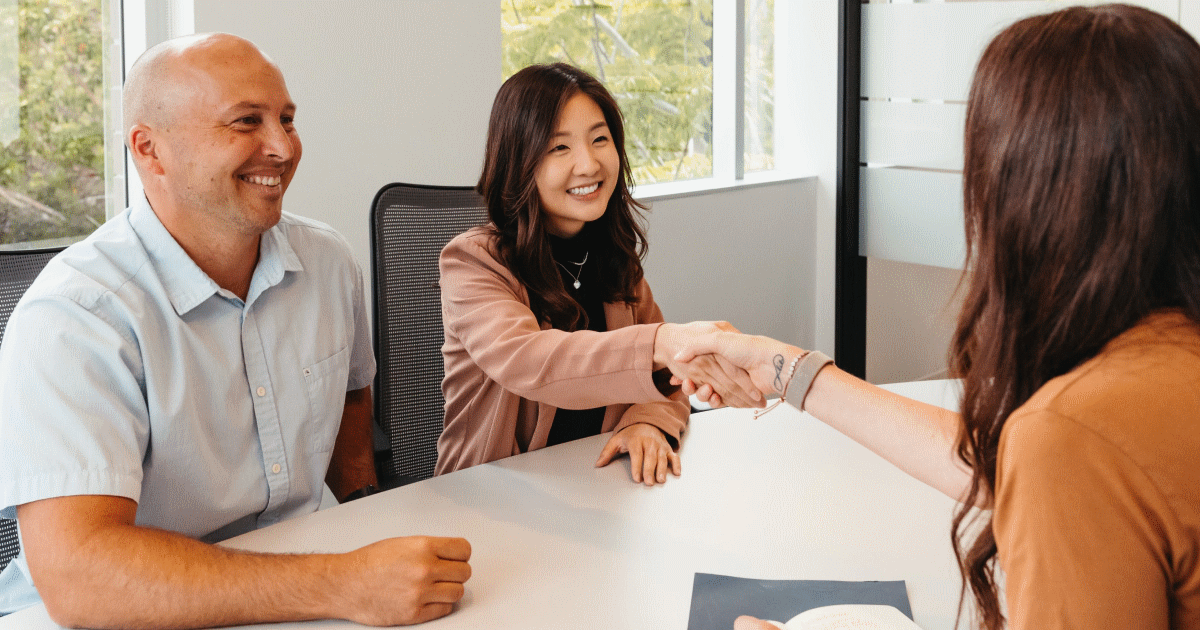 Three people meeting around a table. Two of them are shaking hands.