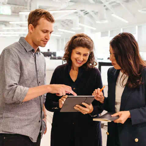 Three people talk and look at a tablet screen.