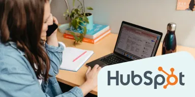 HubSpot logo + an image of woman talking on a mobile while seated at a work desk.