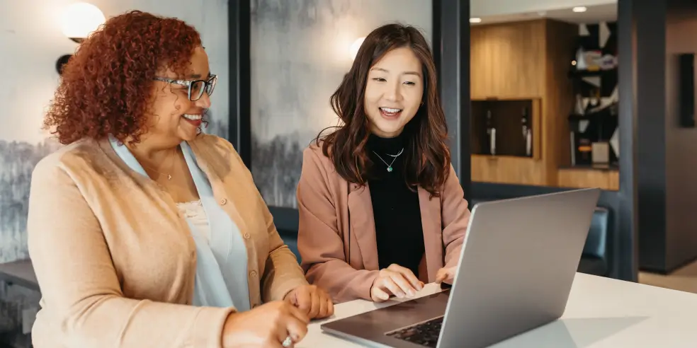 Two office workers seated side by side looking at a laptop screen.