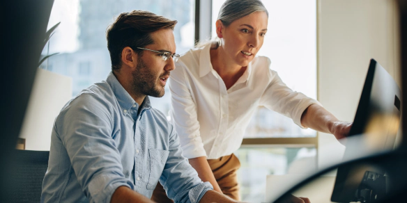 Two coworkers looking at a computer monitor.