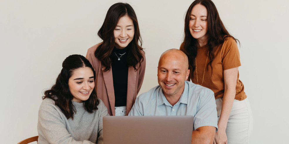 A group of four smiling coworkers looking at a laptop.